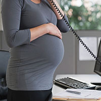 Photo of a pregnant woman standing by a desk and talking on the phone